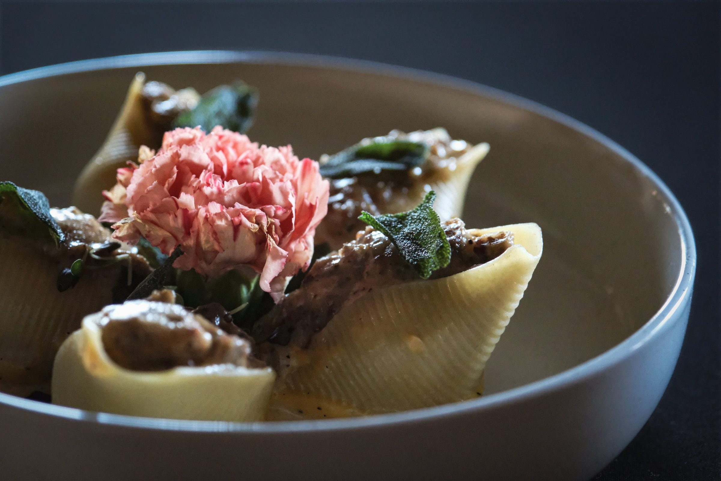 Stuffed pasta shells in a shallow bowl finished with crisp sage and a pink carnation.