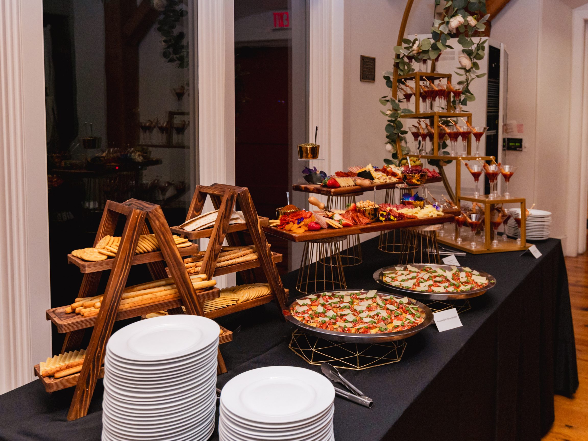 A grazing table of charcuterie, flatbreads and caprese platters with stacked plates.