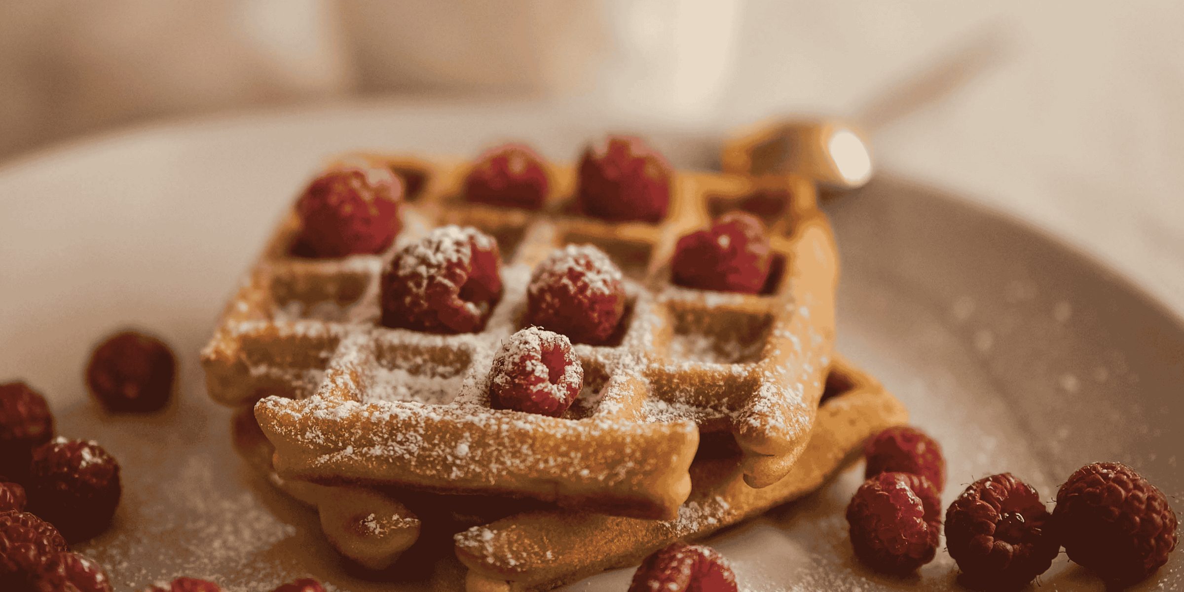 Waffles dusted with sugar and served with fresh raspberries on a pale plate.