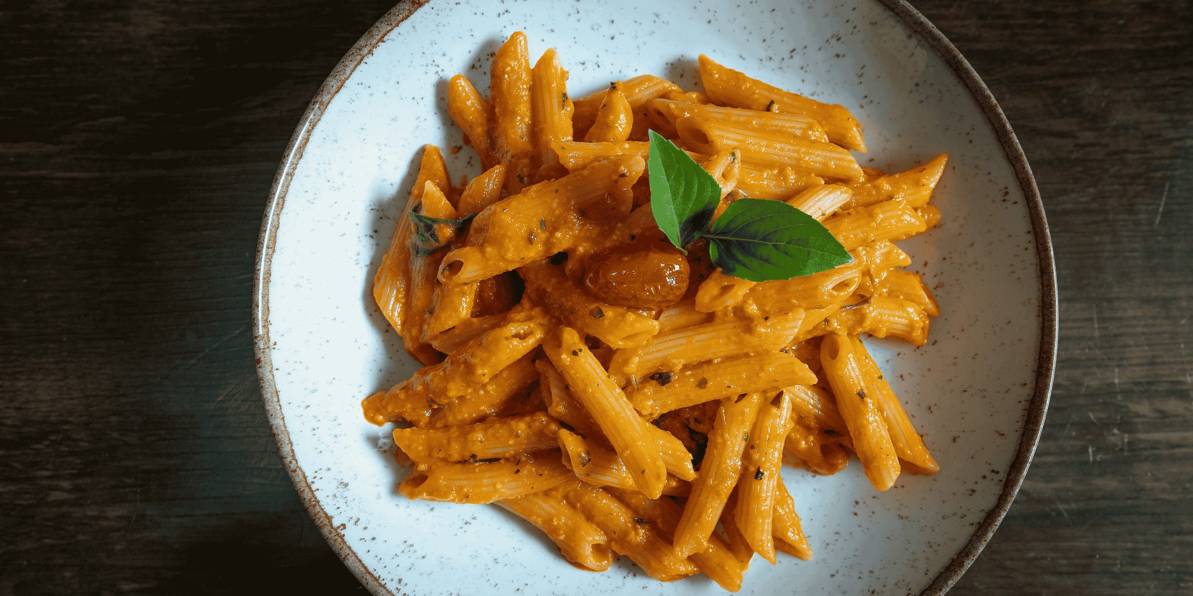 Penne in a creamy tomato sauce topped with fresh basil, served in a pale blue bowl.