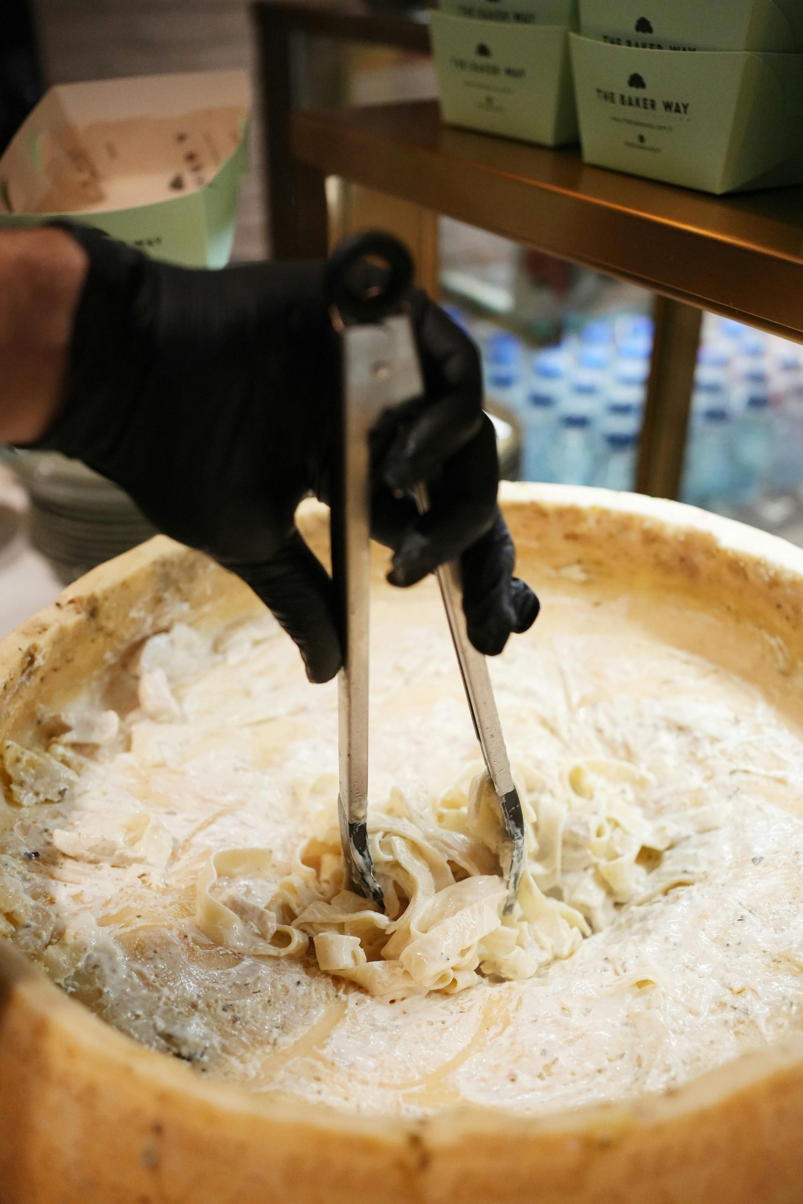 A gloved chef tossing fresh pasta inside a hollowed wheel of cheese.
