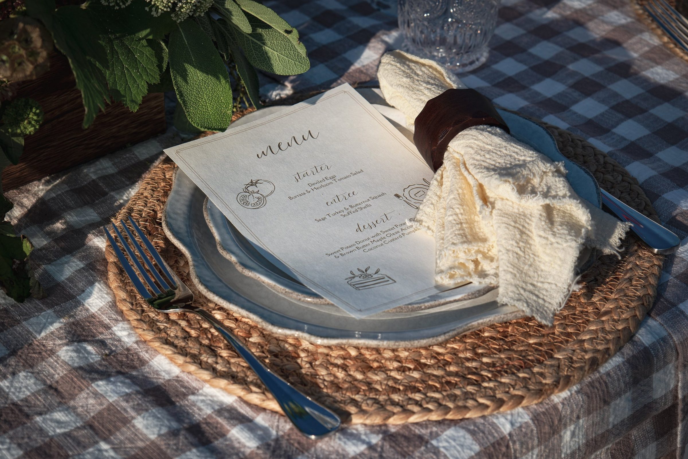 A printed menu card of starter, entree and dessert on a plate at a table laid with a checked cloth.
