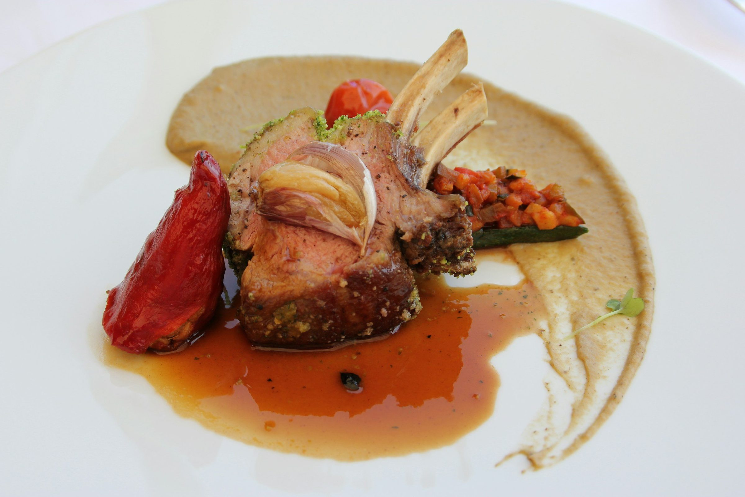 A herb-crusted rack of lamb plated over a smooth puree with a roasted red pepper and pan jus.