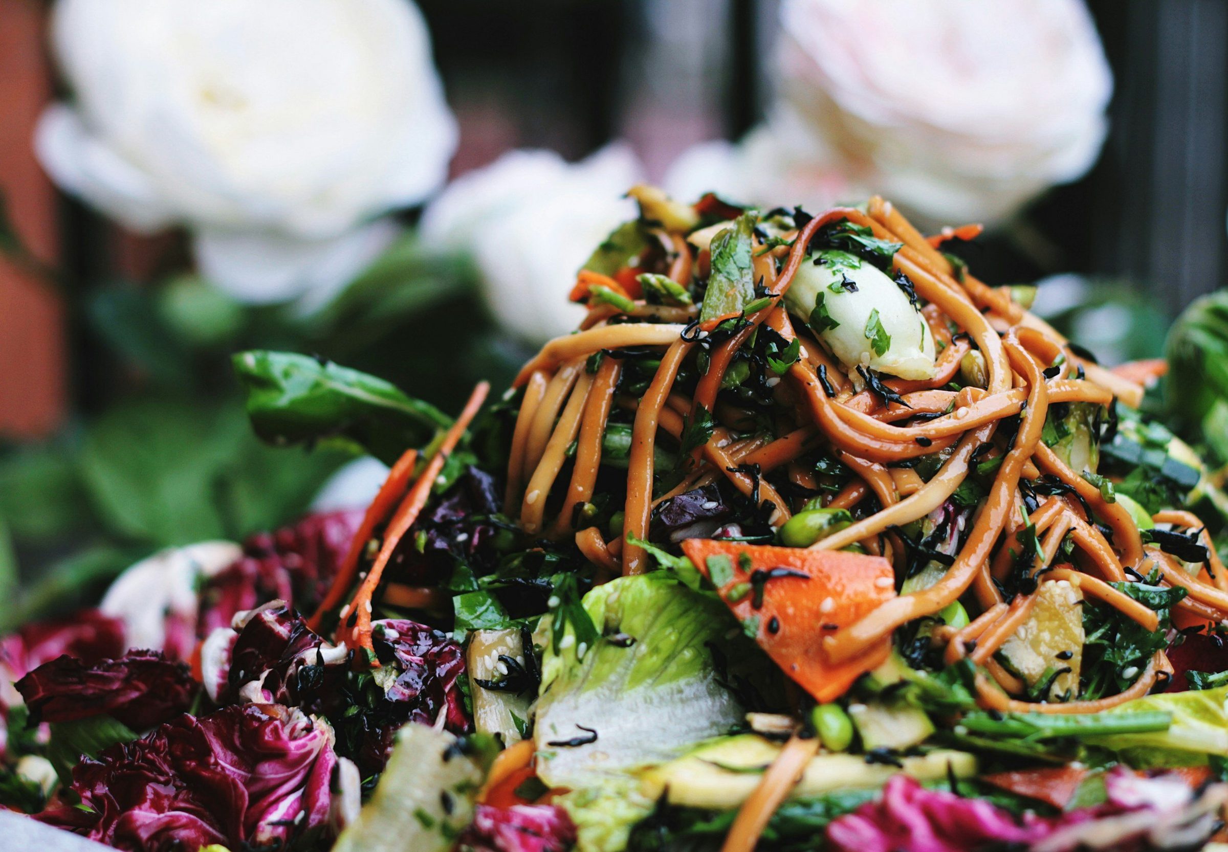 A mounded noodle salad with edamame, shredded carrot, radicchio and sesame seeds.